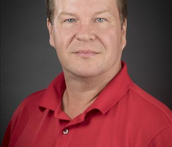 Male employee WITH A RED SHIRT smiling in front of a grey background